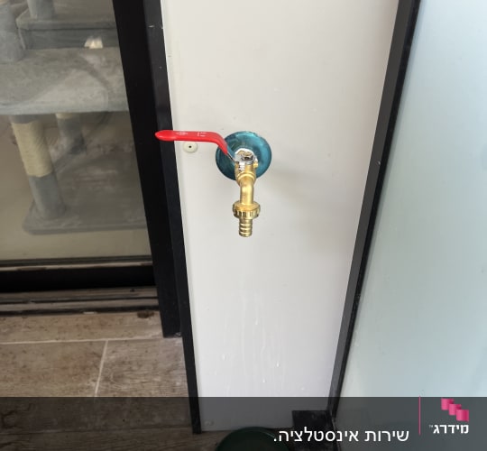 ברז מים עם ידית אדומה על קיר לבן